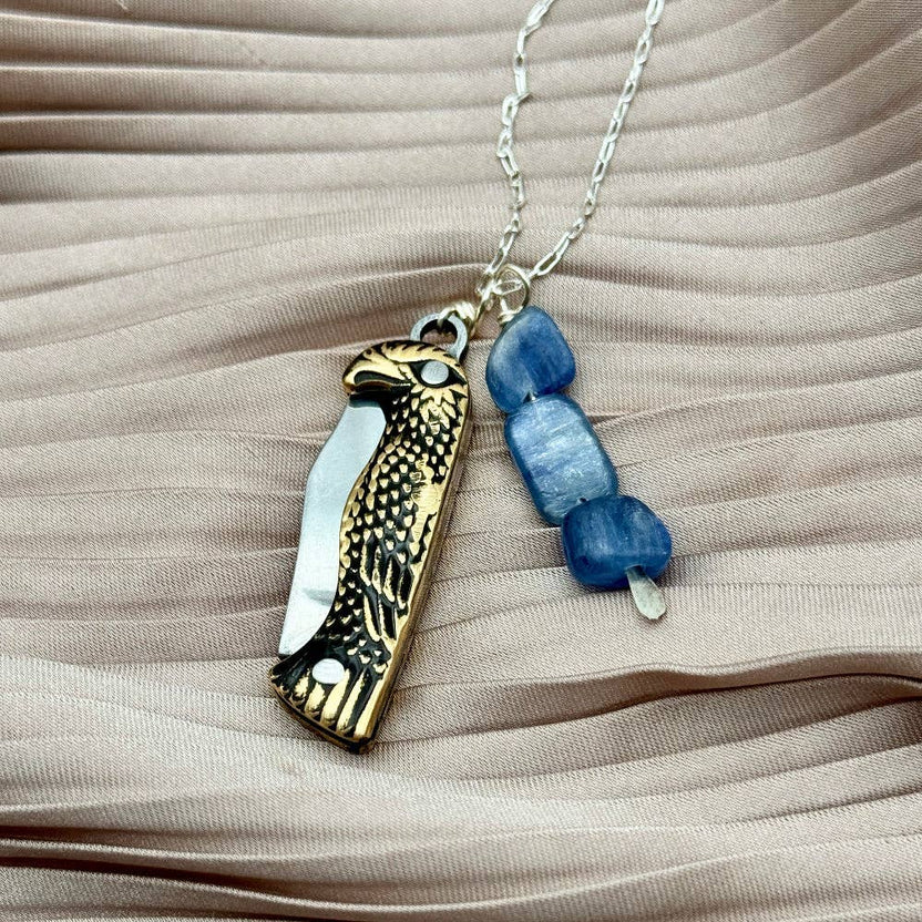 The Talon Necklace by Fluff Hardware is a handcrafted gold-filled necklace featuring an eagle-inspired functional talon utility charm accented with natural kyanite beads. Designed for intentional wear, this mixed-use piece blends symbolic jewelry with practical design. Finished with a hypoallergenic 14k gold filled chain, it’s a bold, meaningful accessory for those drawn to empowered, purpose-driven adornment.
