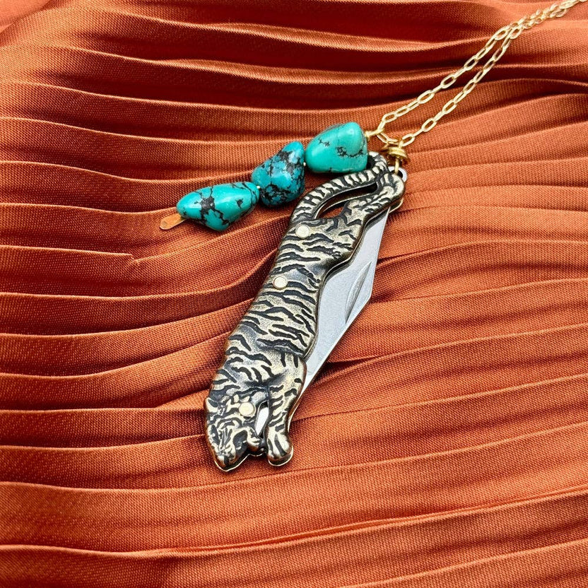 The Untamed Necklace by Fluff Hardware is a handcrafted gold-filled necklace featuring a tiger-inspired functional utility charm accented with natural turquoise nugget beads. Designed for empowered, intentional wear, this small-batch piece blends symbolic jewelry with practical design. Finished on a hypoallergenic 14k gold filled chain, it’s a striking accessory for those drawn to bold craftsmanship and purpose-driven adornment.