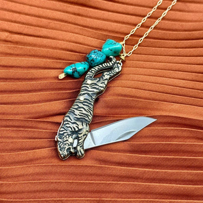 The Untamed Necklace by Fluff Hardware is a handcrafted gold-filled necklace featuring a tiger-inspired functional utility charm accented with natural turquoise nugget beads. Designed for empowered, intentional wear, this small-batch piece blends symbolic jewelry with practical design. Finished on a hypoallergenic 14k gold filled chain, it’s a striking accessory for those drawn to bold craftsmanship and purpose-driven adornment.