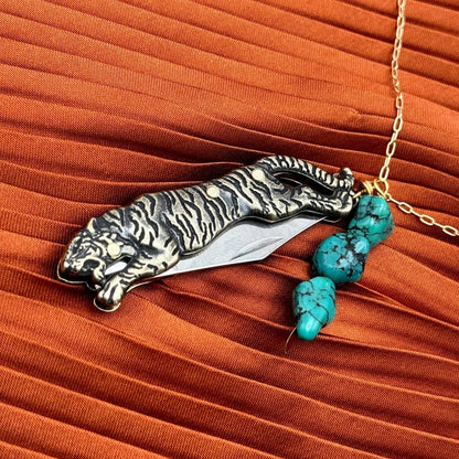 The Untamed Necklace by Fluff Hardware is a handcrafted gold-filled necklace featuring a tiger-inspired functional utility charm accented with natural turquoise nugget beads. Designed for empowered, intentional wear, this small-batch piece blends symbolic jewelry with practical design. Finished on a hypoallergenic 14k gold filled chain, it’s a striking accessory for those drawn to bold craftsmanship and purpose-driven adornment.
