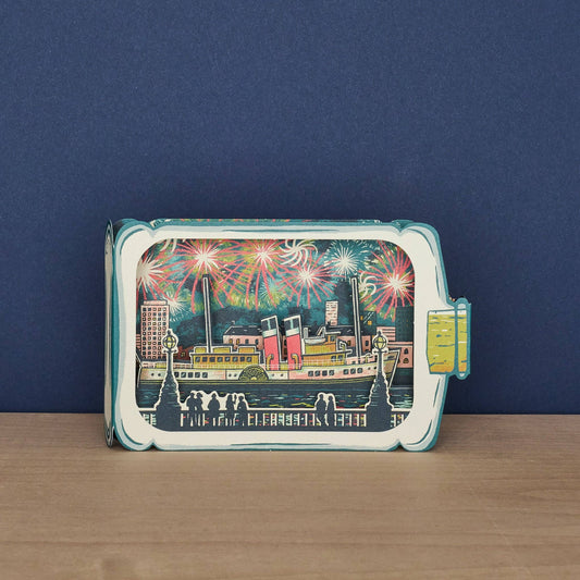 Tom Jay Fireworks Spectacular die-cut greeting card featuring a paddle steamer beneath colorful fireworks inside a bottle-shaped design.